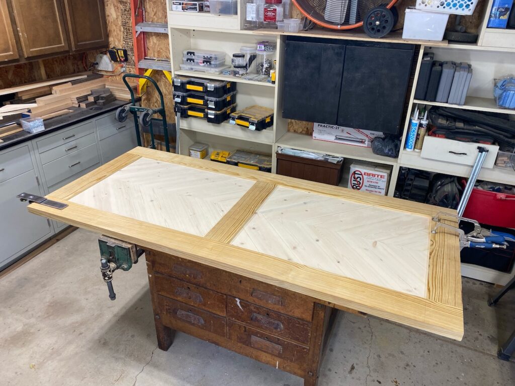 Pine barn door with herringbone pattern on door panels laying on a work bench.