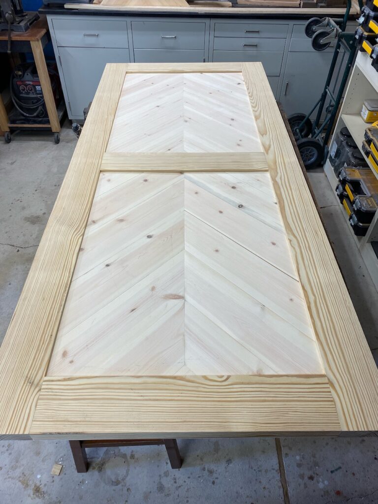 Pine barn door with herringbone pattern on door panels laying on a work bench during the wood bleaching process.