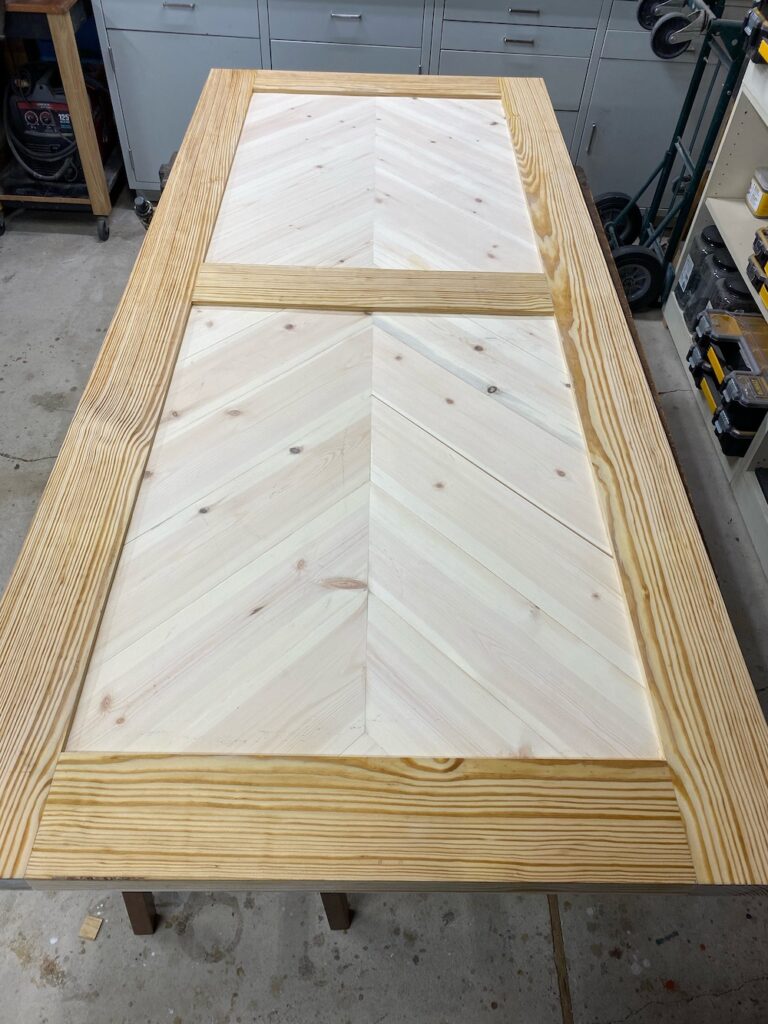 Pine barn door with herringbone pattern on door panels laying on a work bench during the wood bleaching process.